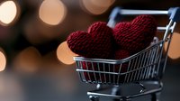 Red knitted heart shapes in miniature shopping cart against blurred bokeh lights background, romantic holiday shopping concept for Valentine's Day.