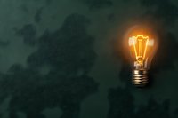 Glowing vintage filament light bulb illuminated on dark green textured background with copy space, symbolizing creativity and innovation in business concept.