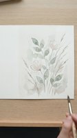 Watercolor floral painting with soft pink flowers and green leaves on white paper, artist hand holding brush creating botanical artwork for home decor and crafts.