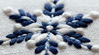 Delicate embroidered snowflake pattern in navy blue and white thread on natural linen fabric, macro close-up showing detailed needlework texture and stitching.