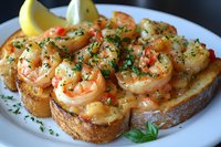 Succulent garlic shrimp on toasted bread garnished with fresh herbs, red pepper flakes and lemon. Closeup of appetizing seafood bruschetta served on white plate.