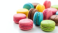 Colorful French macarons in vibrant rainbow hues scattered on white background. Sweet pastry dessert cookies perfect for bakery menu design.