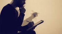 Silhouette of a man in business attire holding a tablet device, hand to chin in thoughtful pose, contemplative professional gesture for corporate concepts.