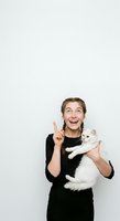 Excited young woman with braided hair holding white fluffy cat, pointing upward against white background. Perfect for pet care, veterinary, animal adoption, and lifestyle marketing materials.