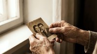 Elderly hands holding vintage black and white photograph of young couple by window, nostalgic memories concept for family history and aging themes.
