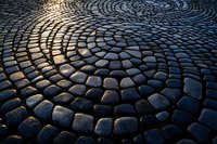 Cobblestone street pattern with sunlight reflection creating dramatic circular texture, wet stone pavement background for architectural design projects.