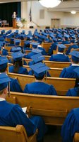Graduation ceremony with students in blue caps and gowns seated in wooden pews listening to speaker at podium in academic hall for commencement celebration.