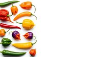 Colorful assorted hot chili peppers arranged on white background. Fresh spicy vegetables including habanero, jalapeno and bell peppers for cooking and seasoning.