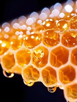 Fresh honeycomb with golden honey dripping in drops, macro close-up view showing hexagonal wax cells structure on black background with bokeh light effect.