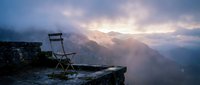 Empty chair on rocky cliff edge overlooking misty mountain valley at dawn, conveying solitude, contemplation, and isolation in nature for editorial and conceptual projects.