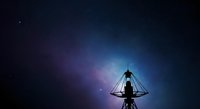 Silhouette of person meditating under geometric wireframe pyramid structure against starry night sky with blue and purple nebula background for spiritual wellness and mindfulness concepts.