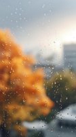 Raindrops on window glass with blurred autumn trees and cityscape in background creating moody atmospheric scene with orange foliage and gray sky.