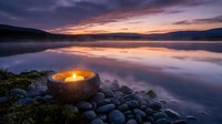 Tranquil lake at sunset with glowing candle in stone bowl on rocky shore. Peaceful meditation and relaxation scene with purple sky reflection on calm water.