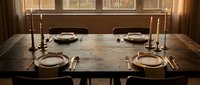 Elegant dining table set for four with ceramic plates, brass candlesticks, and warm lighting creating cozy restaurant or home dining atmosphere.