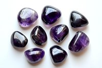Polished amethyst tumbled stones arranged on white background, showcasing deep purple crystal variations and natural mineral formations with glossy surface finish.