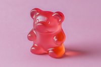 Red translucent gummy bear candy on a soft pink background, close-up macro shot for confectionery, food, and sweet treat concepts.
