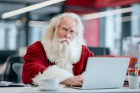 Santa Claus working on laptop computer in modern office environment during Christmas holiday season for business and technology concepts.
