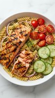 Grilled salmon pasta salad with cherry tomatoes, cucumber slices, red onion and fresh dill in white bowl. Healthy Mediterranean meal for lunch or dinner.