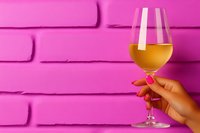 Female hand holding white wine glass against vibrant pink brick wall background, creating modern minimalist composition with bold color contrast.