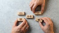 Hands arranging wooden blocks with wellness icons including lotus, heart, dumbbell and leaf symbols for holistic health and lifestyle balance concepts.