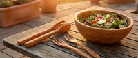 Fresh mixed green salad with vegetables in wooden bowl on rustic table with serving utensils for healthy dining and meal preparation.