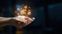Caucasian hand holding glowing golden digital icons and symbols floating above palm against dark background for technology, innovation, and digital transformation concepts.