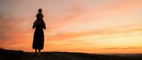 African woman carrying child on shoulders silhouetted against dramatic orange sunset sky, traditional motherhood scene for cultural diversity campaigns.