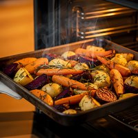 Colorful roasted vegetables with herbs cooking in oven tray with steam rising from hot food preparation for healthy dinner meal.