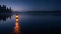 Vintage lantern glowing on calm lake at twilight with forest silhouette and mountain backdrop creating peaceful evening atmosphere for relaxation concepts.
