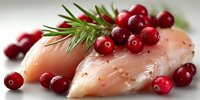 Raw chicken breast fillet garnished with fresh cranberries and rosemary sprig on white plate, ready for holiday cooking preparation.