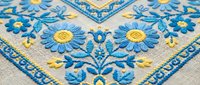 Traditional blue and yellow floral embroidery on linen fabric with decorative border pattern for textile design and craft projects.