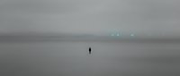 Solitary figure standing in vast misty landscape with distant glowing lights, conveying isolation, mystery, and contemplation for editorial and conceptual projects.