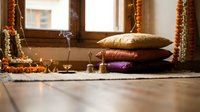 Cozy meditation corner with colorful cushions, brass oil lamp and marigold garlands creating peaceful spiritual atmosphere for yoga and mindfulness practice.