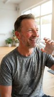 Middle-aged Caucasian man drinking water from a bottle indoors, wearing casual gray t-shirt, suitable for health, fitness, wellness and lifestyle content.