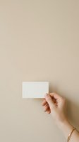 Hand holding blank white business card against neutral beige background, suitable for branding, corporate identity, and marketing mockup designs.