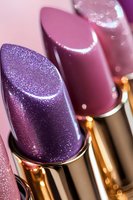 Luxurious purple and mauve lipsticks with metallic shimmer and glitter finish in golden tubes, macro beauty shot showing rich texture and glossy surface.
