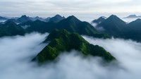 Majestic mountain peaks rise above misty clouds in dramatic aerial landscape, creating ethereal atmosphere with lush green slopes and moody sky. Perfect for nature themes.