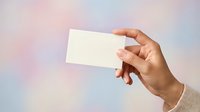 Hand holding blank white business card against soft blurred pastel background, ready for branding, marketing, and corporate identity design projects.