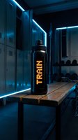 Black carbon fiber sports bottle with glowing yellow text display on wooden bench in modern locker room with neon blue lighting, suitable for athletic and beverage marketing campaigns.