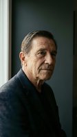 Senior man with gray hair wearing dark sweater poses against neutral background near window for portrait photography, healthcare, lifestyle, and aging-related content.