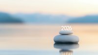 Zen stones stacked with number 2026 on peaceful water surface at sunset. Soft focus meditation background with mountain silhouette reflects serenity and balance.
