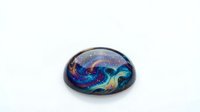 Iridescent glass marble with swirling cosmic colors featuring blue, purple, and gold patterns resembling galaxy or nebula formations on white background.
