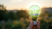 Green energy concept with wind turbines inside glowing light bulb held against sunset landscape for renewable power and sustainability projects.