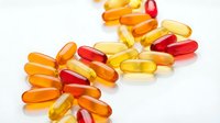 Colorful vitamin capsules and softgels scattered on white background. Health supplements in red, orange and yellow colors isolated for medical design.
