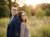 Happy young Caucasian couple wearing glasses posing together outdoors in golden sunset light for professional portrait photography session.