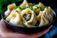 Steamed Asian dumplings filled with meat and vegetables, garnished with fresh chopped green onions served in black ceramic bowl, close up food photography.