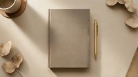 Closed beige linen notebook with blank pages next to gold pen, dried flowers and straw hat on neutral background, suitable for stationery and lifestyle design projects.