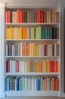 Elegant white bookshelf with colorful books arranged in rainbow order, creating a vibrant spectrum display against classic architectural elements.