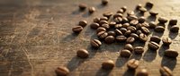 Roasted coffee beans scattered on rustic wooden surface with warm lighting creating shadows and texture for cafe branding and beverage marketing materials.