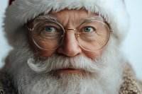 Close up portrait of senior man with white beard and round glasses wearing Santa hat, showing warm genuine smile and twinkling blue eyes. Festive holiday concept.